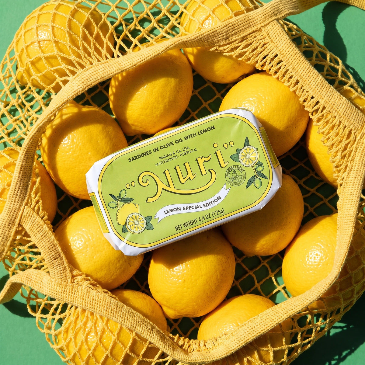 Nuri Sardines in Olive Oil with Lemon surrounded by whole lemons in grocery bag
