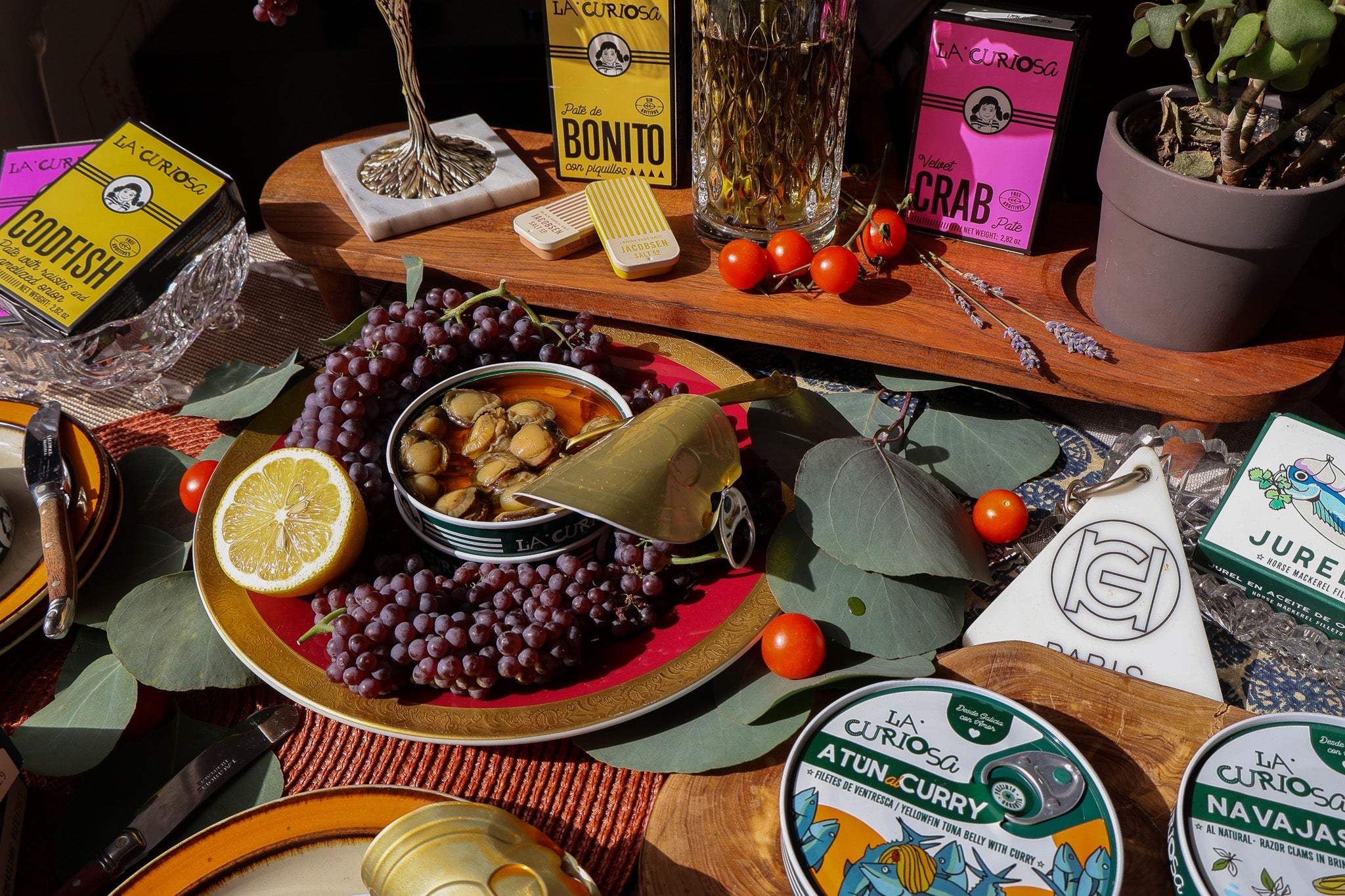 Elaborate spread of tinned fish, lemons, vegetables, tomatoes and decorative elements like glasses of wine and leaves