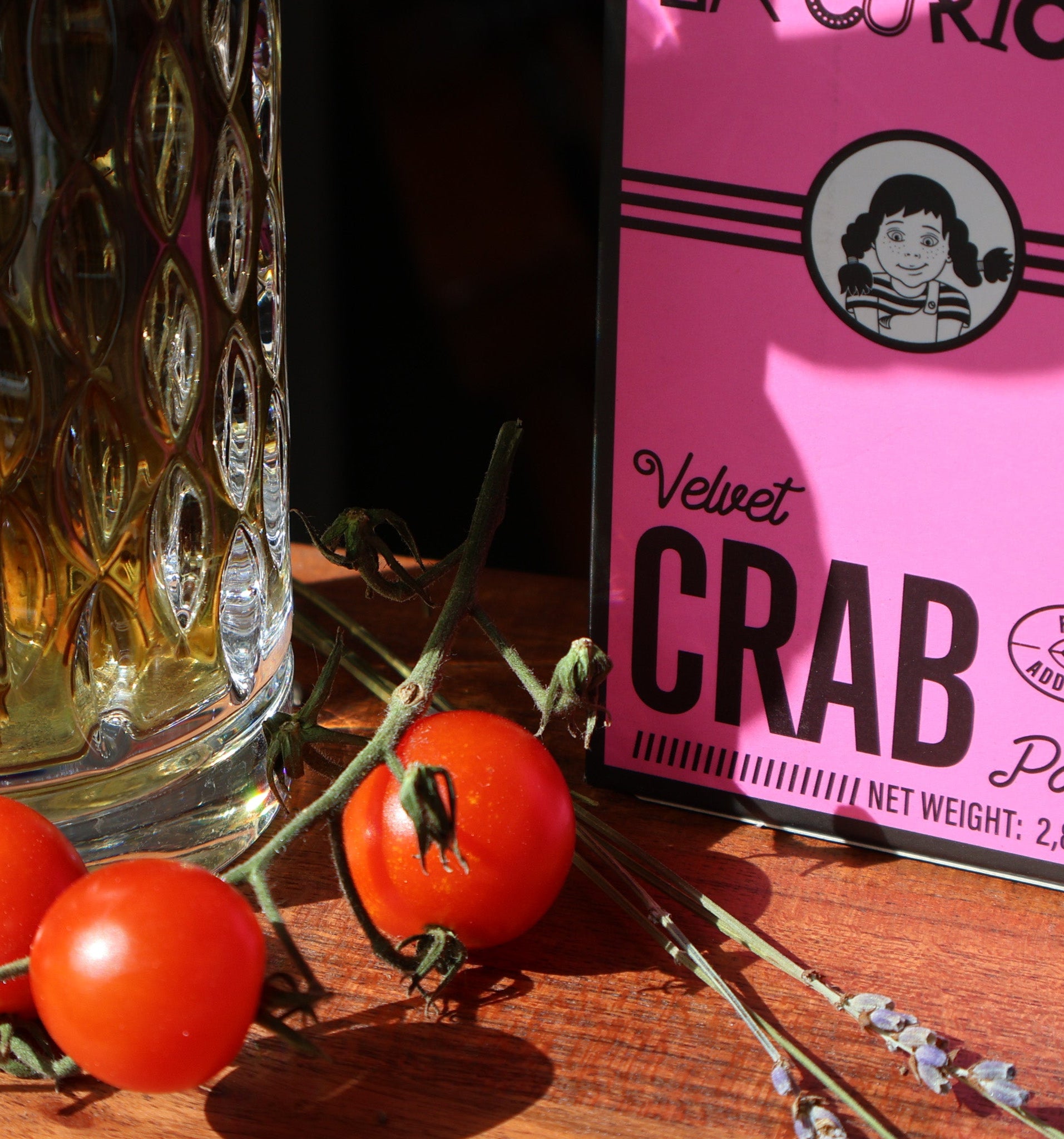 Pink can of 'Velvet Crab' pate with cherry tomatoes and a glass jar on a wooden surface