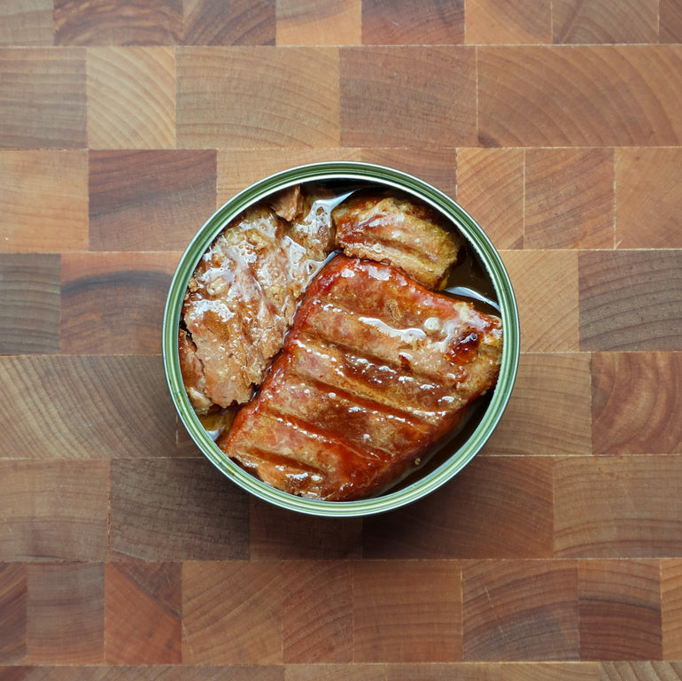 Open Güeyu Mar chargrilled tin on a walnut butcher block showing grill marks and rich olive oil